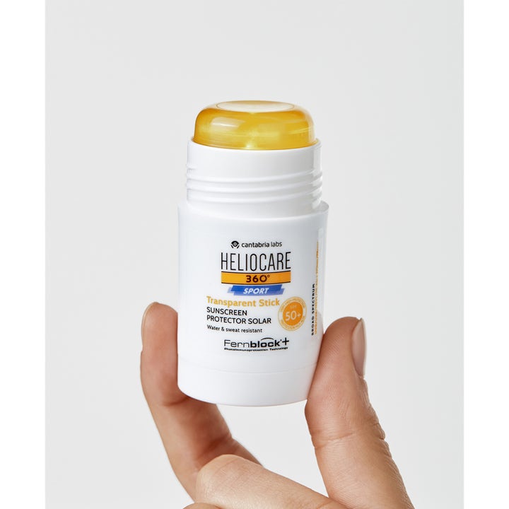 Heliocare Sport Stick SPF 50+ 25 g vandafvisende solcreme i hvid stift med gennemsigtig gul balm holdt i en hånd