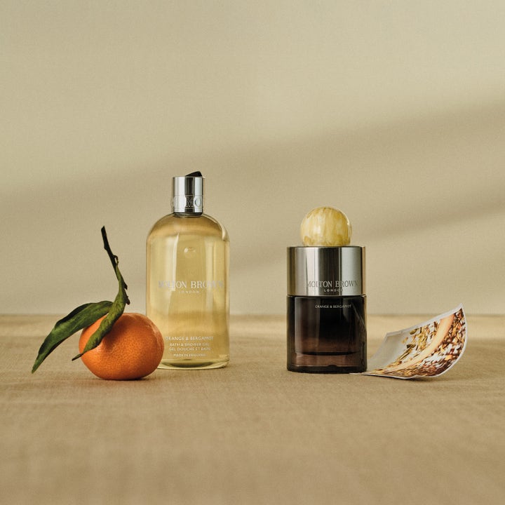 Molton Brown Orange & Bergamot 300 ml opfriskende showergel i klar flaske ved siden af en frisk appelsin