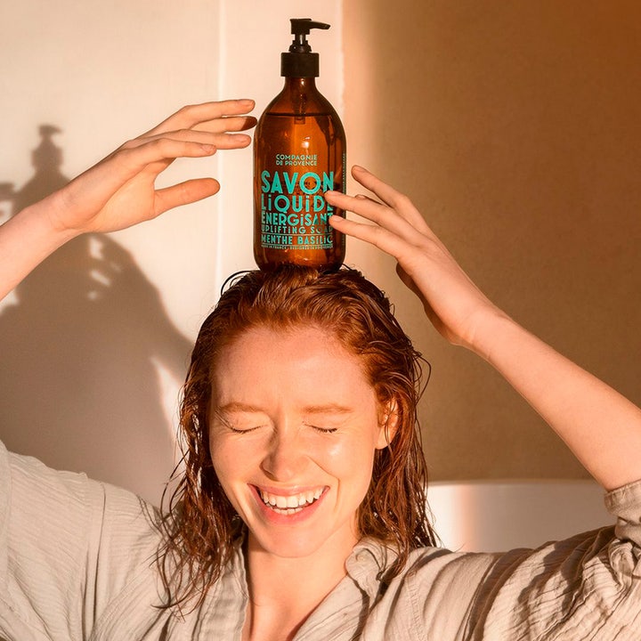 Compagnie de Provence Liquid Marseille Soap Mint Basil 495 ml energigivende håndsæbe på hovedet af smilende kvinde.