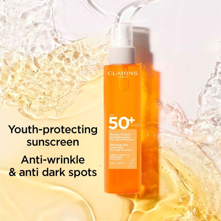 Clarins Glowing Sun Care Mist 150 ml solcreme SPF 50+ mod rynker i orange sprayflaske omgivet af gyldne vandstænk.