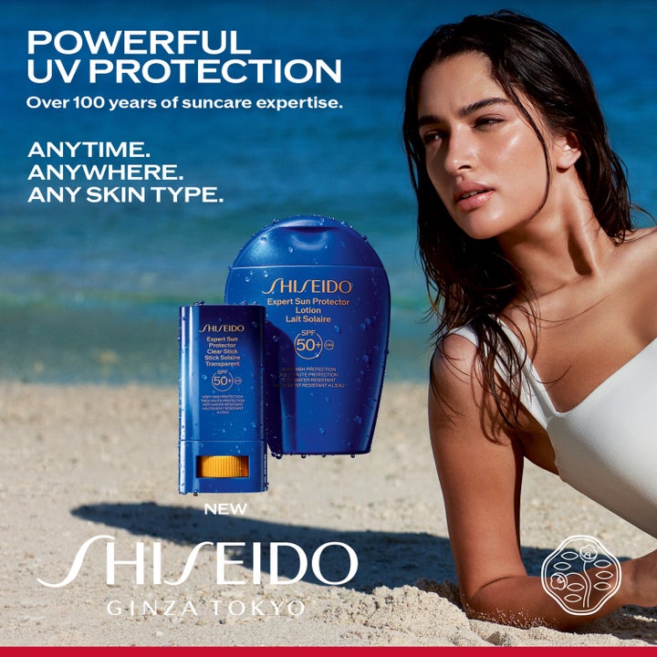 Shiseido Global Sun Care Clear Stick 20 g solbeskyttelse i blå hylster vist på en strand med en kvinde ved havet.
