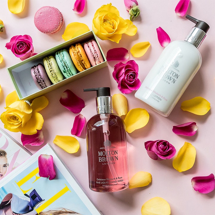 Molton Brown Delicious Rhubarb & Rose Hand Lotion 300 ml fugtgivende håndcreme vist med rosenblade og macarons.