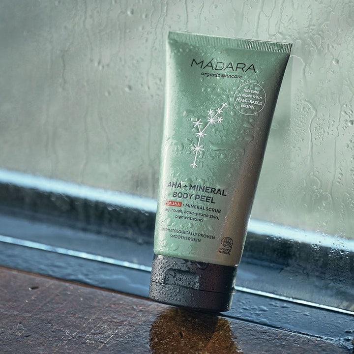 MÁDARA AHA + Mineral Body Peel 175 ml eksfolierende kropspeeling i grøn tube i et fugtigt miljø