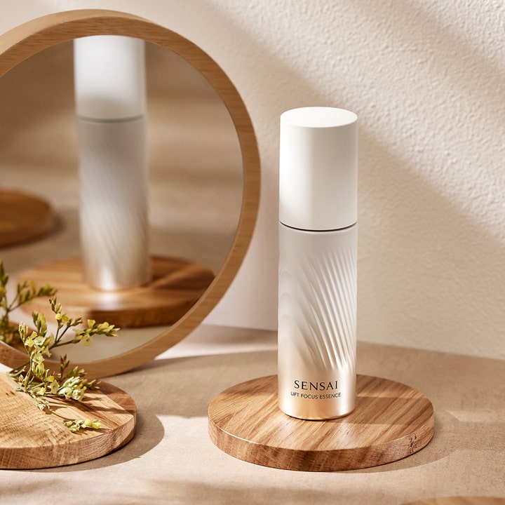 Sensai Lift Focus Essence 40 ml opstrammende serum i hvid og guld flaske på en træbase foran et spejl