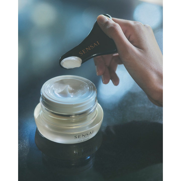 Sensai Ultimate The Mask 75 ml anti-age ansigtsmaske med fyldig creme på en sort spatel over en frostet glaskrukke