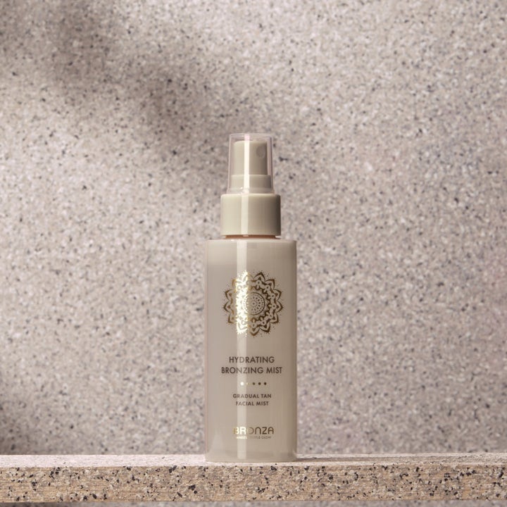 Bronza Hydrating Bronzing Mist Duo 2 x 100 ml fugtgivende selvbruner i beige sprayflaske med guldlogo på sten.