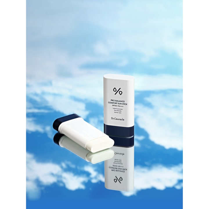 Dr. Ceuracle Pro Balance Sun Stick 18 g solcreme i hylster på en spejlende overflade med blå himmel og skyer.