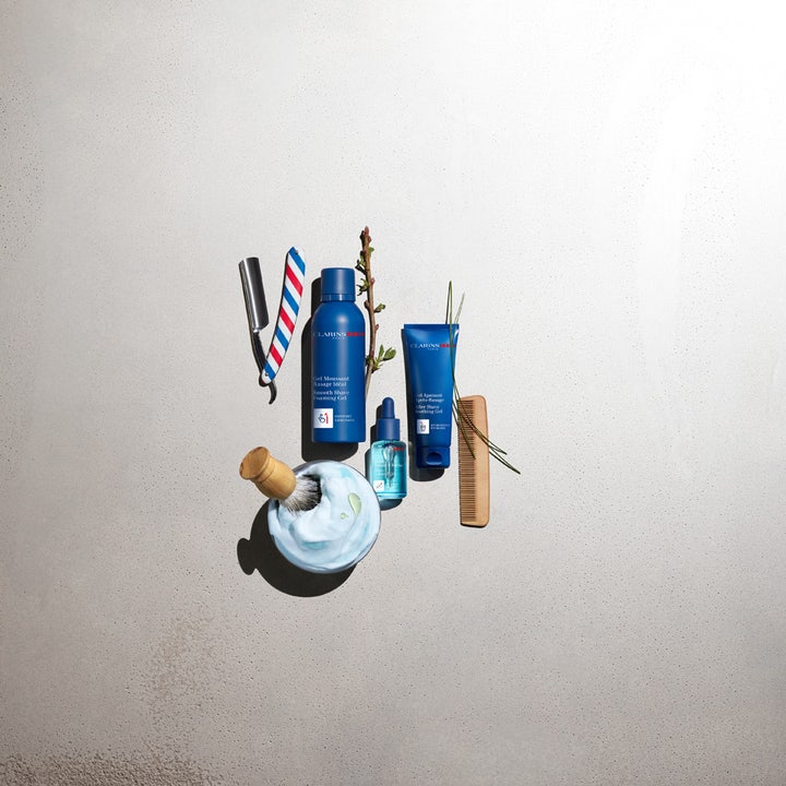 Clarins Men Shave Gel 150 ml plejende rakgel i blå emballage omgivet af barberudstyr og skum på grå baggrund