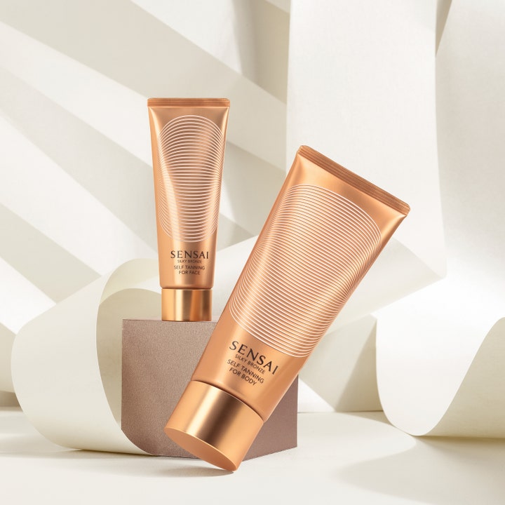 Sensai Silky Bronze Self Tanning For Face 50 ml giver glød i kobberfarvet tube på podie med hvide papirstrimler.