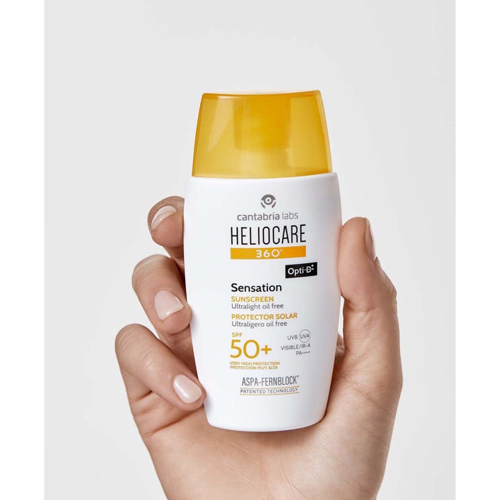 Heliocare Sensation SPF 50+ 50 ml ultralet solcreme til ansigtet i hvid flaske med gult låg holdt i en hånd