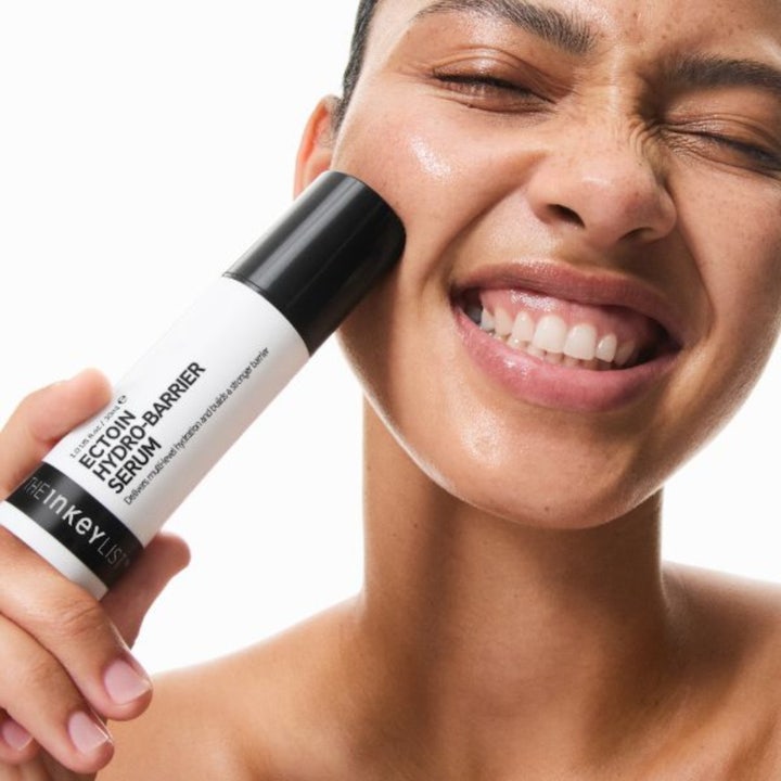 The INKEY List Ectoin Hydro-Barrier Serum 30 ml fugtgivende serum holdes mod kinden af en smilende kvinde med glød.