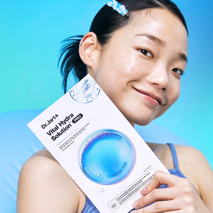 Dr.Jart+ Dermask Vital Hydra Solution Pro 26 g ansigtsmaske holdes af smilende kvinde på blå baggrund
