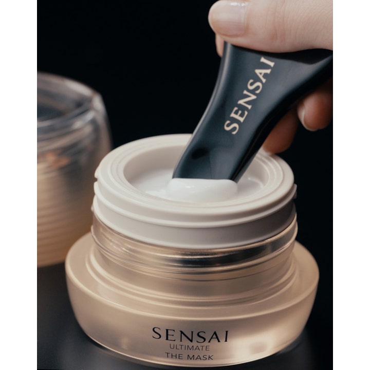 Sensai Ultimate The Mask 75 ml plejende ansigtsmaske i guldfarvet glaskrukke med cremet hvid tekstur og sort spatel