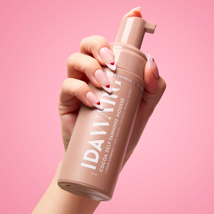 IDA WARG Cocoa Self-Tanning Mousse 150 ml giver glød i brun flaske holdt af hånd mod pink baggrund