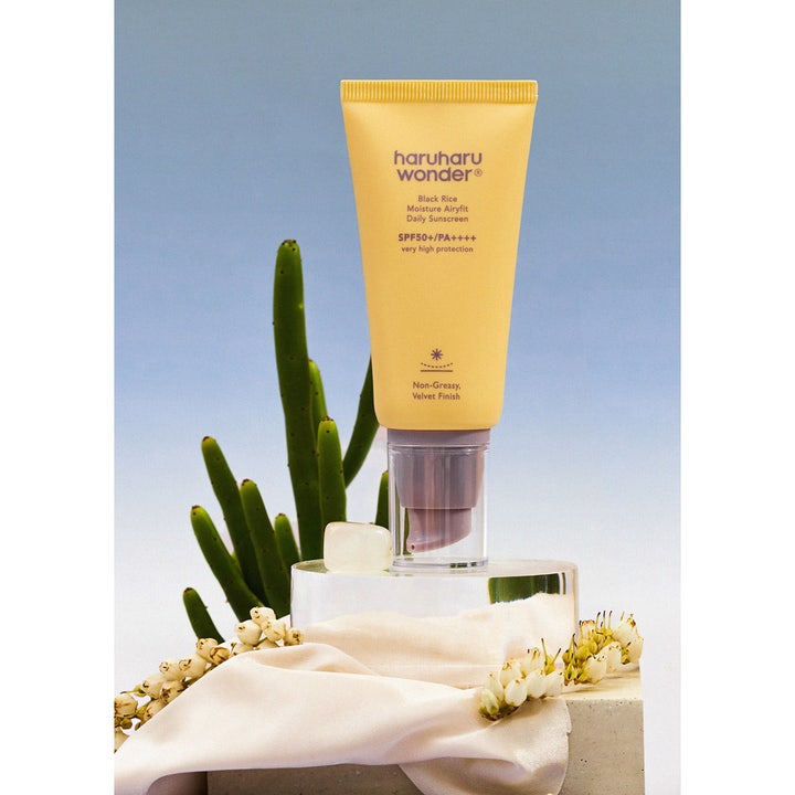 Haruharu Wonder Black Rice Daily Sunscreen 50 ml SPF 50 gul tube på glaspiedestal med hvide blomster og grøn kaktus.