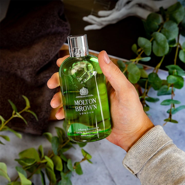 Molton Brown Infusing Eucalyptus Bath & Shower Gel 300 ml opfriskende duschtvål i en hånd med eukalyptusblade