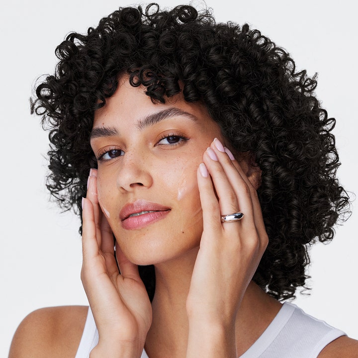 Clinique Moisture Surge 100H 50 ml fugtgivende ansigtscreme påføres af kvinde med mørke krøller.