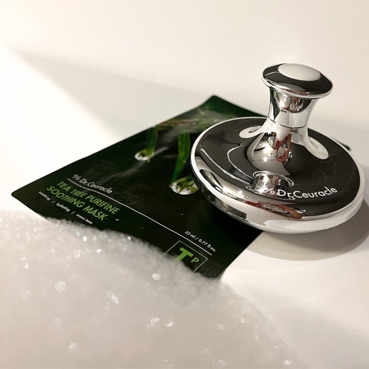 Dr. Ceuracle Cryo Tool 1 stk kølende ansigtsværktøj i blankt sølv placeret på en grøn Tea Tree sheet mask
