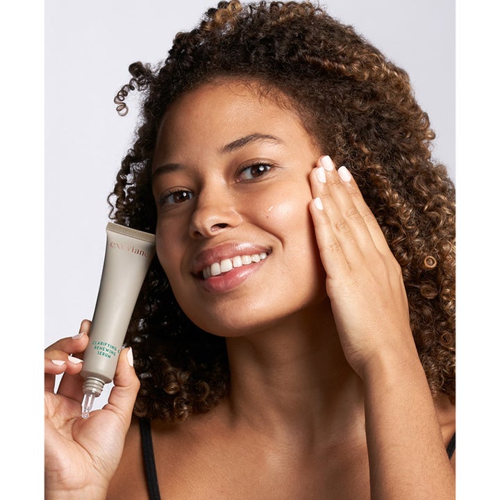 Exuviance Clarifying and Renewing Serum 30 ml fornyende ansigtsserum vist af en smilende kvinde med tuben mod huden