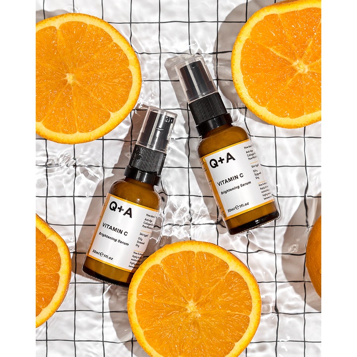 Q+A Vitamin C Brightening Serum 30 ml lysnende ansigtsserum i brune glasflasker omgivet af friske appelsiner i vand