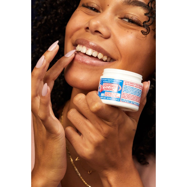 Smilende kvinde holder Egyptian Magic All Purpose Skin Cream 59 ml fugtgivende ansigtscreme i hvid krukke