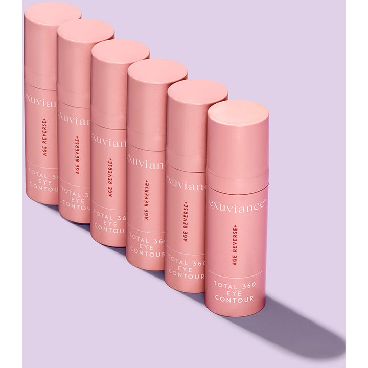 Exuviance Age Reverse Eye Contour 15 g anti-aging øjencreme i seks lyserøde beholdere på række mod lilla baggrund