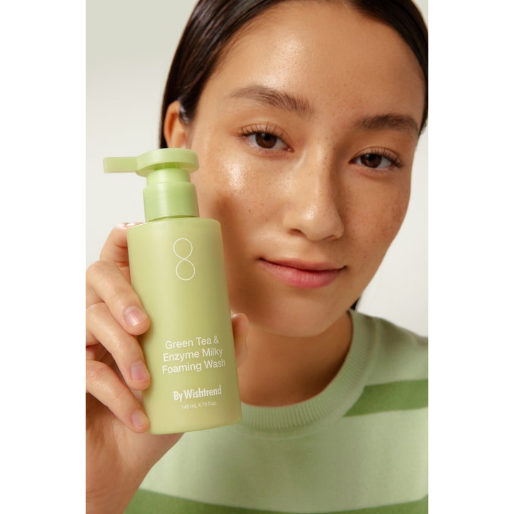 By Wishtrend Green Tea & Enzyme Milky Foaming Wash 140 ml ansigtsrens i lysegrøn pumpeflaske holdt af en kvinde