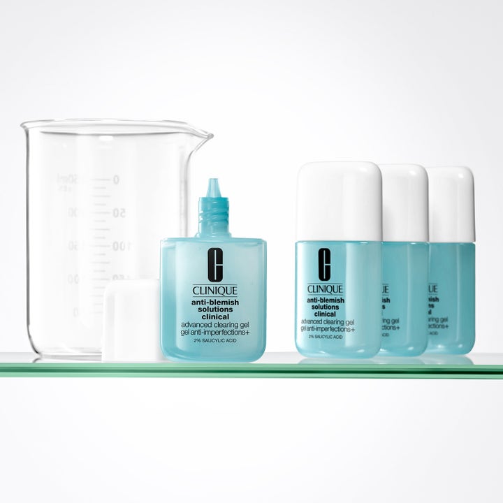 Clinique Anti-Blemish Solutions Clinical 20 ml mod urenheder i lyseblå flasker med salicylsyre ved en glaskolbe