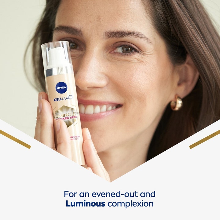 NIVEA LUMINOUS 630 Tinted Fluid 40 ml dagcreme mod mørke pletter holdt af smilende kvinde for en jævn hudtone.