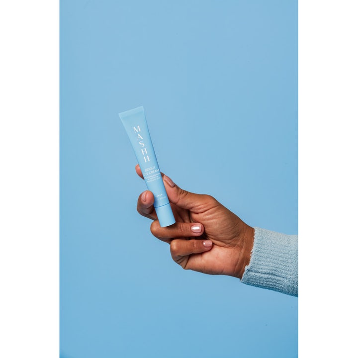 MASHH Bright Eye Cream 15 ml fugtgivende øjencreme med peptider i lyseblå tube holdt mod blå baggrund.