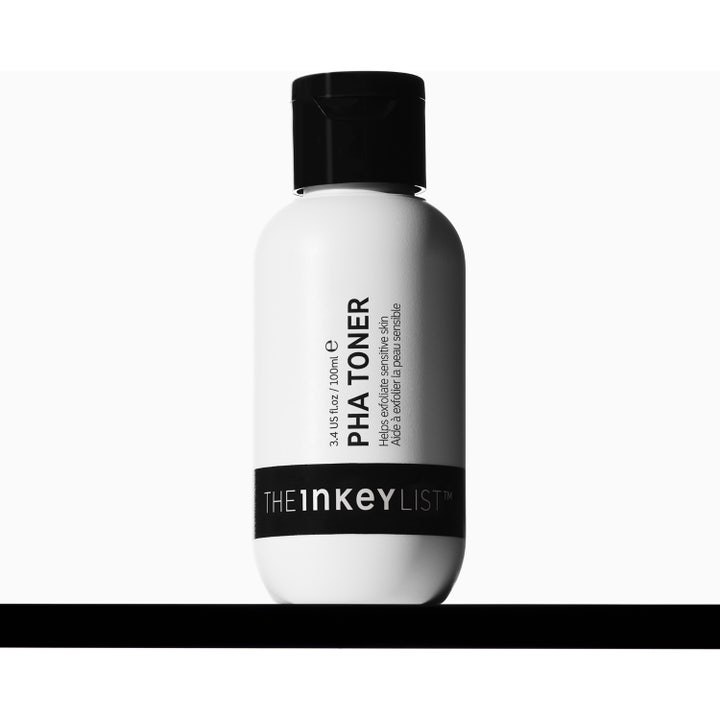 The INKEY List PHA Toner 100 ml eksfolierer sensitiv hud i hvid flaske omgivet af vandstænk mod lilla baggrund.