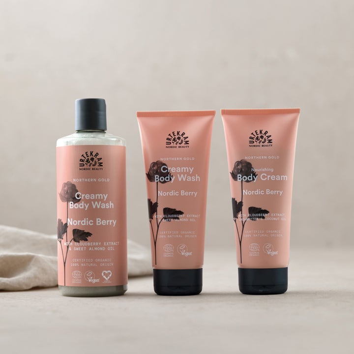 Urtekram Nordic Berry Creamy Body Wash 500 ml kropsvask i rosa flaske og tuber med sorte låg i et roligt miljø.