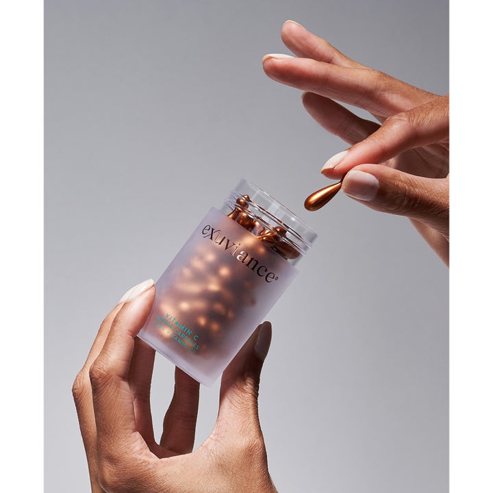 Exuviance Vitamin C Serum Capsules 60 stk glødgivende serum i krukke holdt af hænder med en bronze kapsel.
