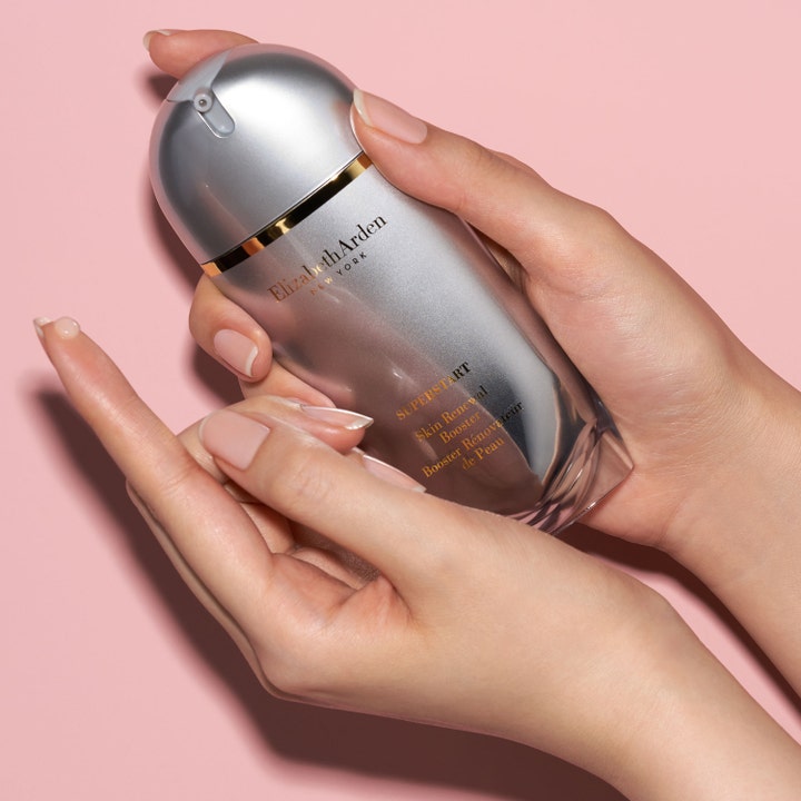 Elizabeth Arden Superstart Skin Renewal Booster 50 ml serum i sølvflaske holdt i hænder mod lyserød baggrund