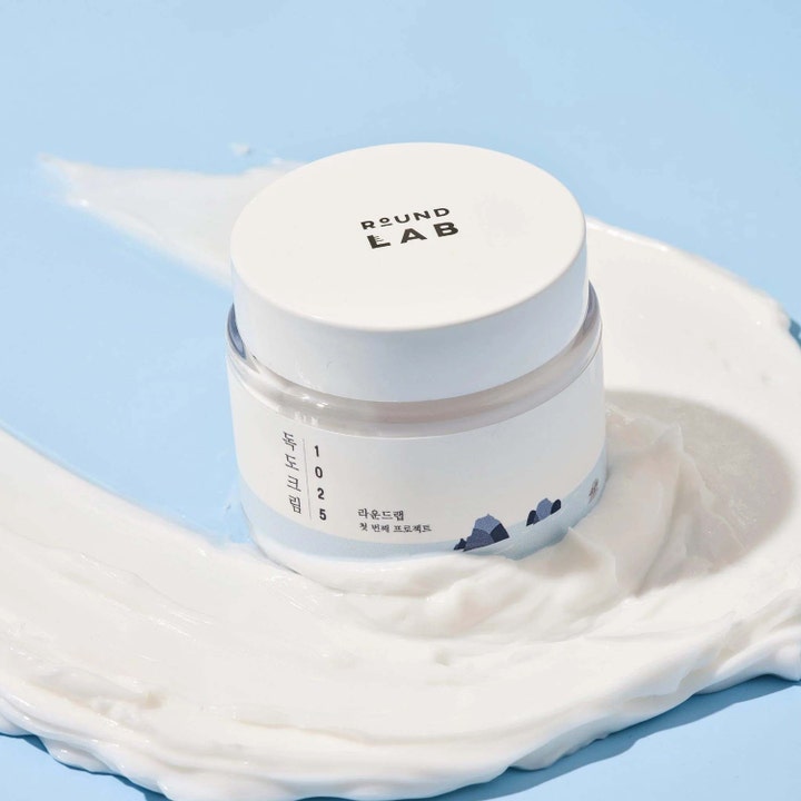 Round Lab 1025 Dokdo Cream 80 ml fugtgivende ansigtscreme i krukke omgivet af hvid cremet tekstur