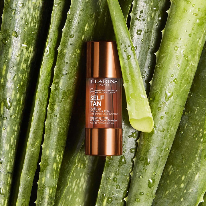 Clarins Radiance-Plus Golden Glow Booster 15 ml tanning drops i bronzefarvet flaske omgivet af grønne aloe vera-blade