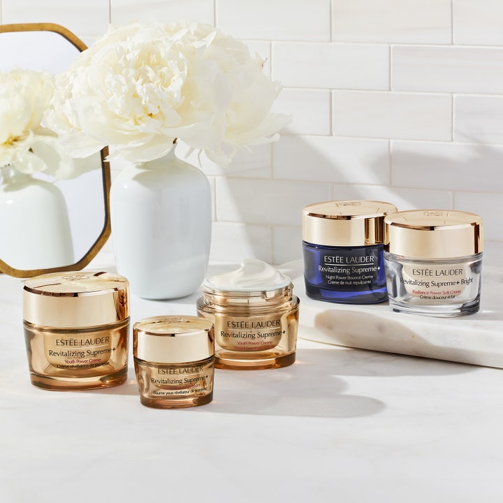Estée Lauder Revitalizing Supreme+ Bright 50 ml ansigtscreme der giver glød i sølvkrukke med guldlock ved hvide blomster