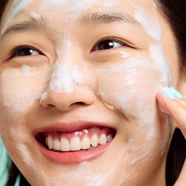 Dr.Jart+ Pore-remedy Renewing Foam Cleanser 150 ml ansigtsrens på en smilende kvinde med hvidt skum og blå korn