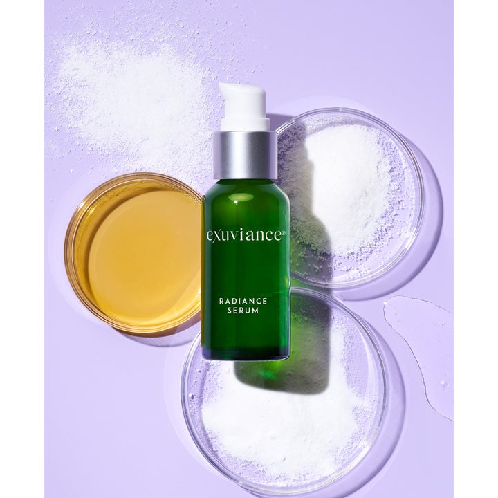 Exuviance Radiance Serum 30 ml glødgivende ansigtsserum i grøn glasflaske med ingredienser i petriskåle