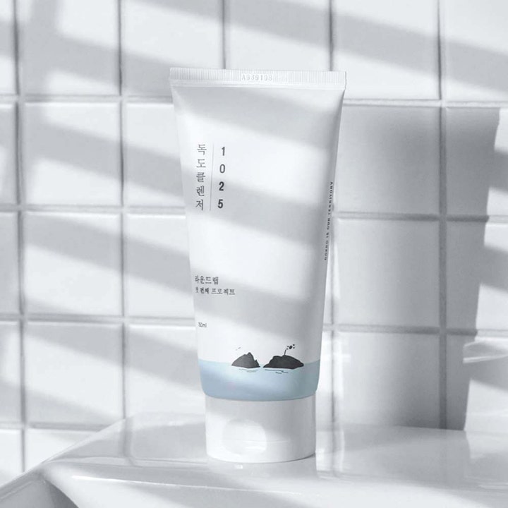 Round Lab 1025 Dokdo Cleanser 150 ml fugtgivende ansigtsrens i hvid tube med blå detaljer foran hvide fliser