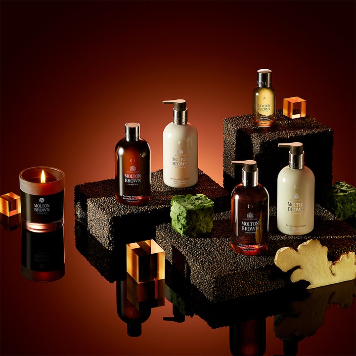 Molton Brown Black Peppercorn Body Lotion 300 ml fugtgivende hudpleje vist i et varmt setup med lys og krydderier.
