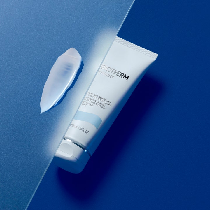 Biotherm Biomains 100 ml fugtgivende håndcreme i tube ved siden af cremet tekstur på blå baggrund