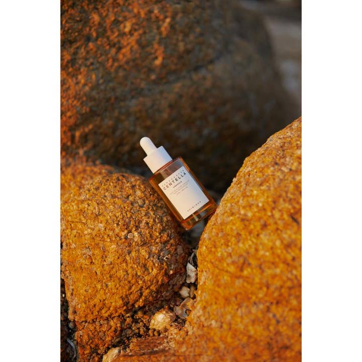 SKIN1004 Madagascar Centella Ampoule 55 ml beroligende serum i glasflaske placeret på gyldne klipper