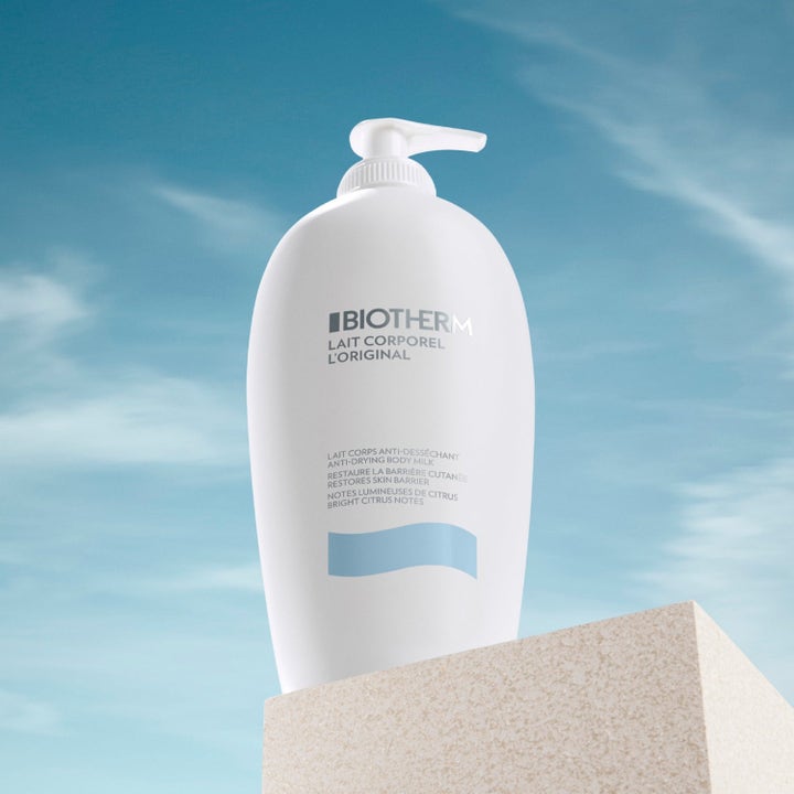 Biotherm Lait Corporel 400 ml fugtgivende bodymilk i hvid pumpeflaske på en lys stenblok mod en blå sommerhimmel.