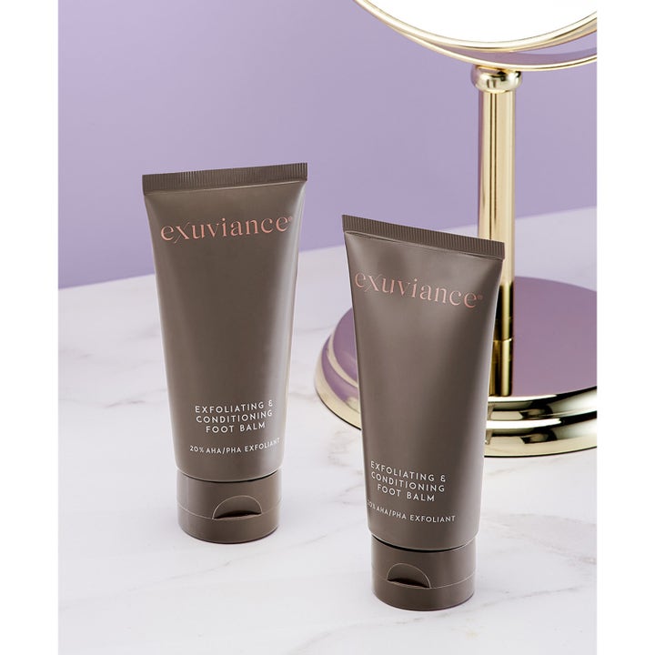 Exuviance Exfoliating & Conditioning Foot Balm 50 g eksfolierende fodcreme i to brune tuber ved et spejl