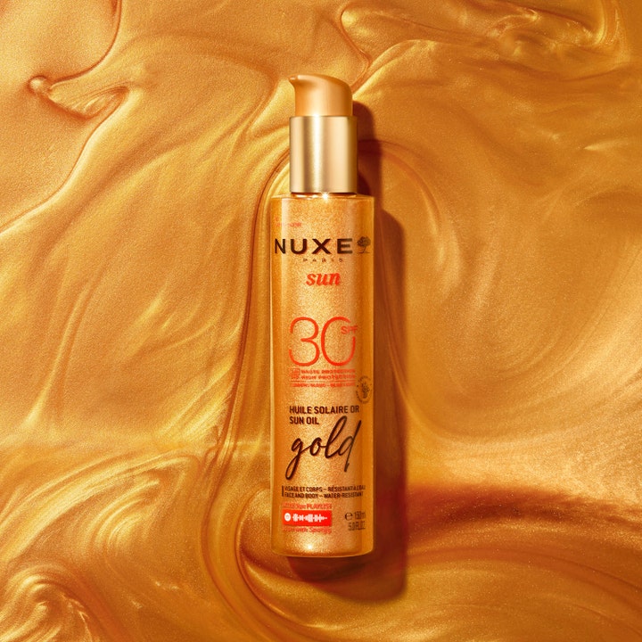 Nuxe Sun Tanning Oil Gold 150 ml beskyttende sololie SPF30 i guldpumpeflaske på en bølgende guldoverflade.