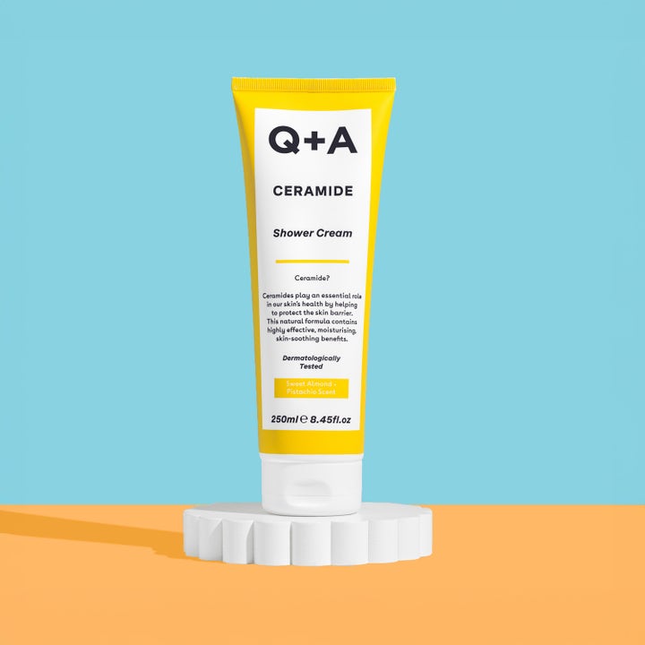 Q+A Ceramide Shower Cream 250 ml fugtgivende badecreme i gul tube stående på en hvid piedestal.
