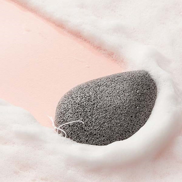 Purito Bamboo Charcoal Konjac Sponge 7 g giver en dybderensende eksfoliering med grå porøs svamp i hvidt skum.