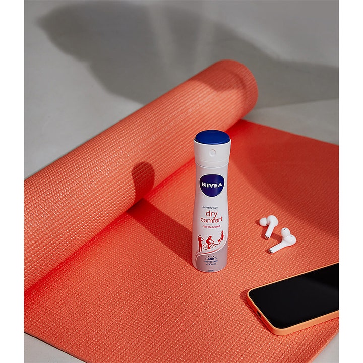 NIVEA Dry Comfort 150 ml deospray der giver beskyttelse på en koralrød yogamåtte med høretelefoner.