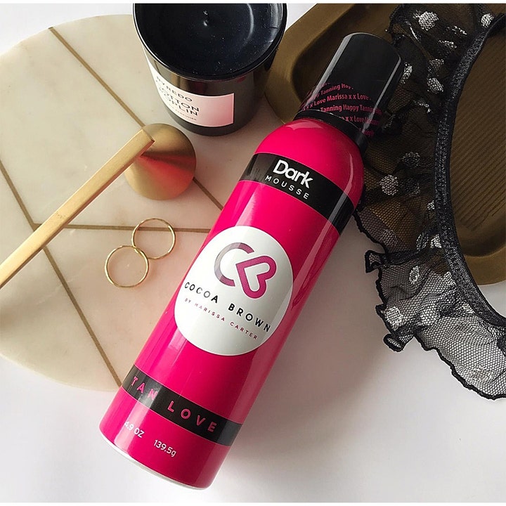 Cocoa Brown 1 Hour Tan Dark 150 ml selvbruner mousse i pink flaske ved siden af et duftlys
